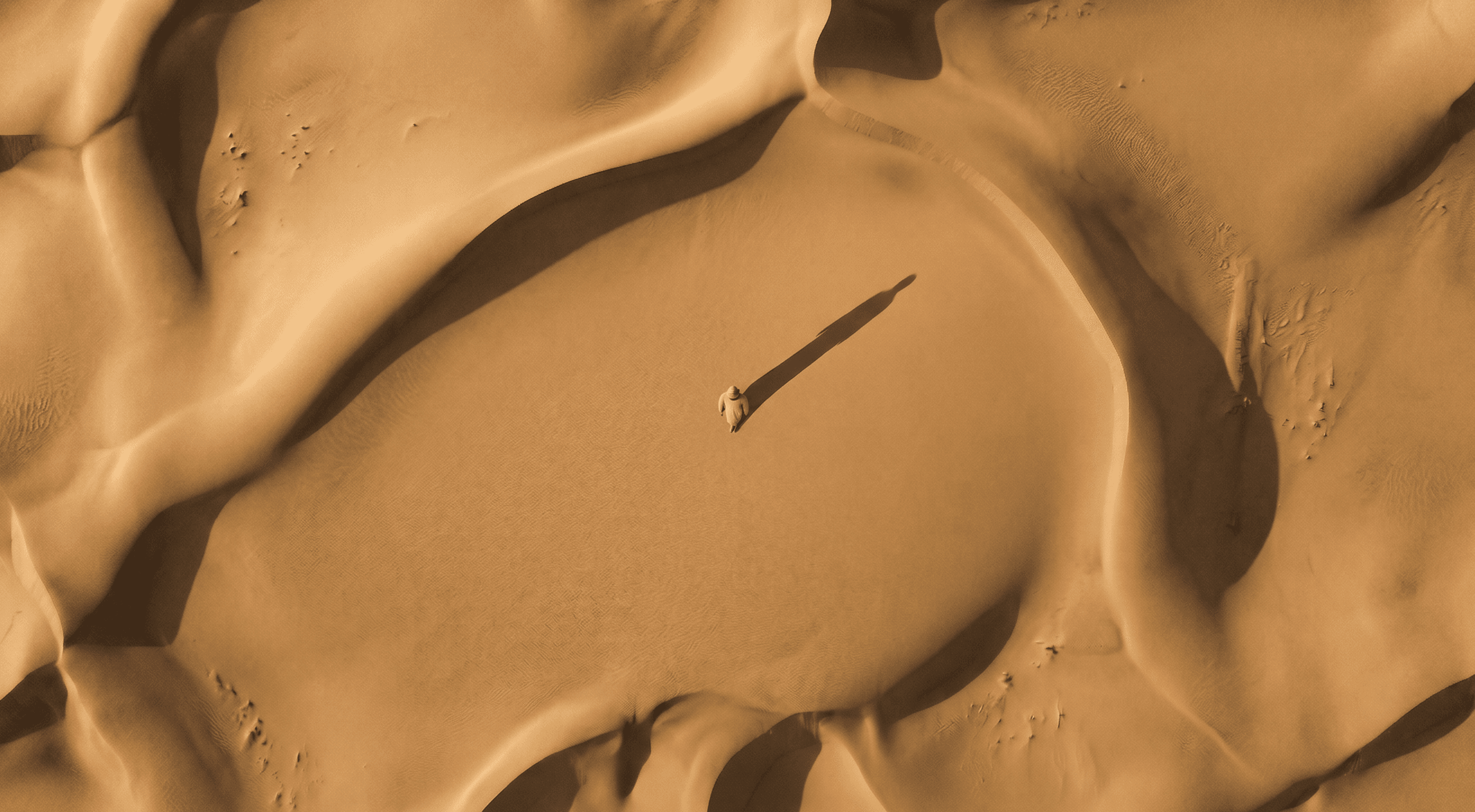 Aerial view of a lone traveller crossing vast desert dunes